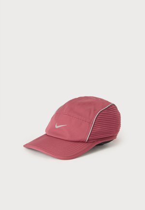 Casquette de sport Nike rose avec une visière incurvée et un logo swoosh blanc, avec des panneaux texturés côtelés et un passepoil blanc sur les côtés.