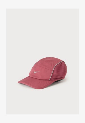 Casquette de sport Nike rose avec une visière incurvée et un logo swoosh blanc, avec des panneaux texturés côtelés et un passepoil blanc sur les côtés.