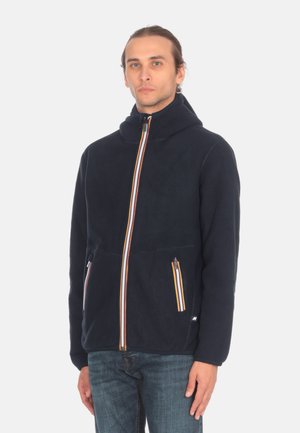 Giacca in pile blu navy con colletto alto, due tasche con zip e una zip frontale con strisce multicolori. Tessuto morbido, design casual.
