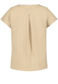 Chemise beige à manches courtes avec un large décolleté et un pli inversé unique au centre du dos.