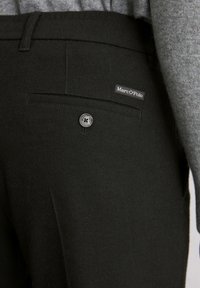 Pantalons en laine noir avec une finition texturée, dotés d'une fermeture à bouton, d'une poche arrière et d'une petite étiquette "Marc O'Polo" sur la taille.