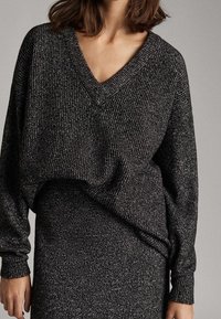 Dunkelgrauer, strukturiert gestrickter Pullover mit V-Ausschnitt, langen Ärmeln und lockerem Schnitt, kombiniert mit einem passenden Bleistiftrock aus ähnlichem Material.