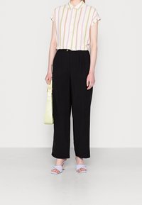 Camicia a maniche corte con bottoni, a righe verticali rosa e verdi, abbinata a pantaloni neri a vita alta. Gli accessori includono una borsa verde chiaro e sandali lilla.