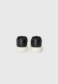 Sneaker nere in pelle texture con suola in gomma bianca a contrasto e pannello posteriore. Presentano un design elegante e minimale. Nessun motivo visibile.
