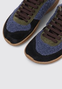 Baskets basses avec un tissu texturé bleu, des bouts de chaussure en daim noir, des œillets en daim vert olive, des lacets marron et des semelles en caoutchouc couleur gomme.