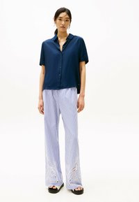 Camisa de botones de manga corta en color navy con una textura brillante, combinada con pantalones de pierna ancha a rayas que presentan detalles florales bordados en blanco.