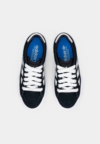 Black suede sneakers with white laces and three white stripes. Blue insoles with "adidas" branding visible. White rubber soles.