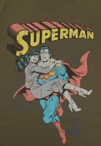 Camiseta gráfica que presenta a Superman con un traje azul y rojo, sosteniendo a una mujer con un vestido gris, sobre un fondo oliva con el texto "Superman" en negrita.