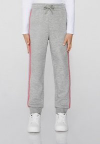 Graue Sweatpants mit einem Kordelzugbund, ausgestattet mit pinken und silbernen seitlichen Streifen und elastischen Bündchen. Kombiniert mit weißen Sneakers.