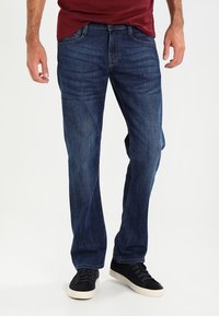 Blå denimjeans med rak passform, urtvättad textur, femfickorsdesign och spänne, tillsammans med svarta sneakers.