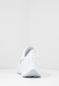 Scarpa sportiva bianca con una tomaia in tessuto a texture liscia e logo swoosh grigio, suola imbottita e un design del tallone leggermente curvato.