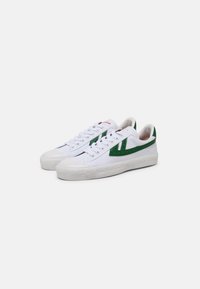 White canvas sneakers with a green textured side logo, round toe, white laces, and a textured rubber sole. Red accent on the tongue.