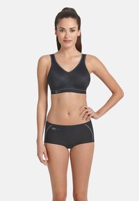 Zwarte sport-bh met een V-hals en brede banden, gecombineerd met zwarte boyshorts met contrasterende stiksels. Gladde textuur, minimaal ontwerp.