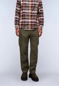 Karierte Langarmbluse in Rot-, Grün- und Blautönen. Olivgrüne Cargohose mit Seitentaschen. Schwarze Schuhe vervollständigen das Outfit.