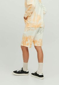 Pomarańczowe i białe szorty w stylu tie-dye wykonane z miękkiego materiału, z elastycznym pasem i bocznymi kieszeniami, połączone z czarnymi tenisówkami i szarymi skarpetkami.