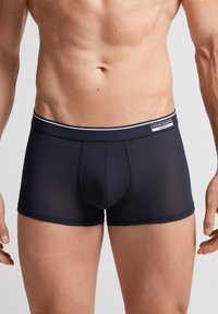 Mörkblå trunk-stil kalsonger med en mjuk, elastisk midjeband som har ett vitt streck och en logotypetikett. Slät, stretchig tyg, figurnära design.