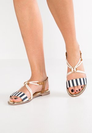 Striped flat sandals with braided rope straps and a metallic base. Features a circular accent and open toe design. Colors include navy and white.
