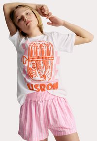 Witte t-shirt met oranje sardineprint en de tekst "LISBOA," gecombineerd met roze gestreepte shorts. Ontspannen pasvorm, ronde halsontwerp, zachte stof.