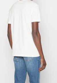 Camiseta de algodón blanca con mangas cortas, corte relajado y escote redondeado; combinada con jeans de mezclilla azul claro, mostrando un estilo casual.