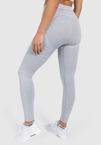 Leggings grises de talle alto con un patrón texturizado y un ajuste ceñido, combinados con zapatillas deportivas blancas. Enfocados en la funcionalidad y la comodidad.