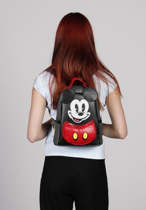 Mochila de imitación de cuero negro con diseño de Mickey Mouse con orejas redondas y un bolsillo frontal rojo, destacando detalles en color amarillo.