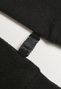 Black plastic side-release buckle connecting two black textured fabric straps on a light surface.