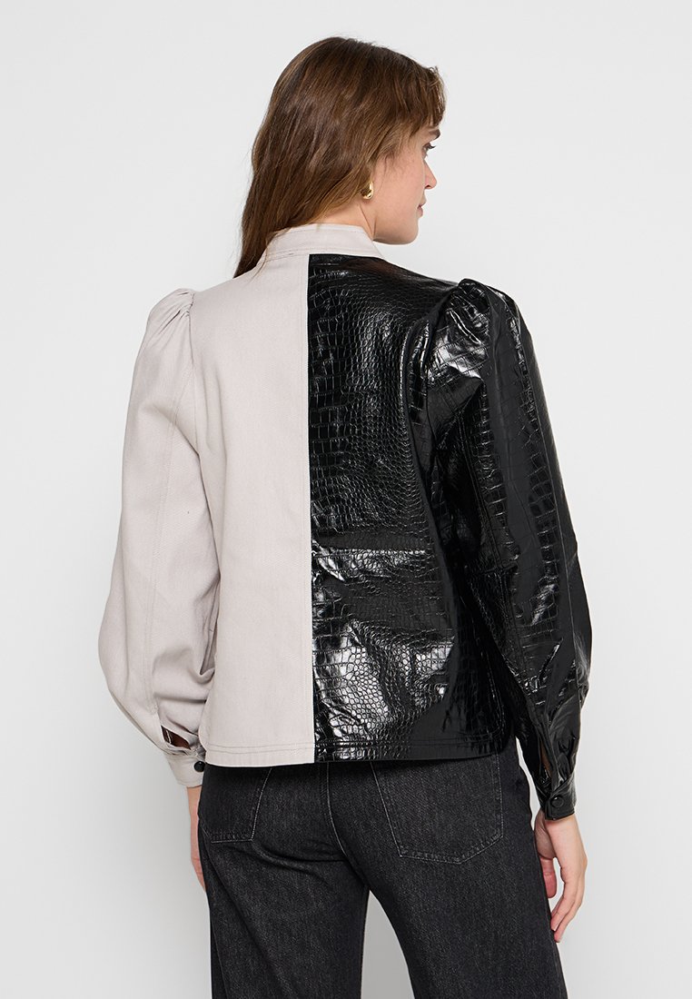Dwukolorowa kurtka z jasnoszarym materiałem po jednej stronie i czarną lakierowaną skórą z imitacji krokodyla po drugiej, z puffnymi rękawami i miękką teksturą.