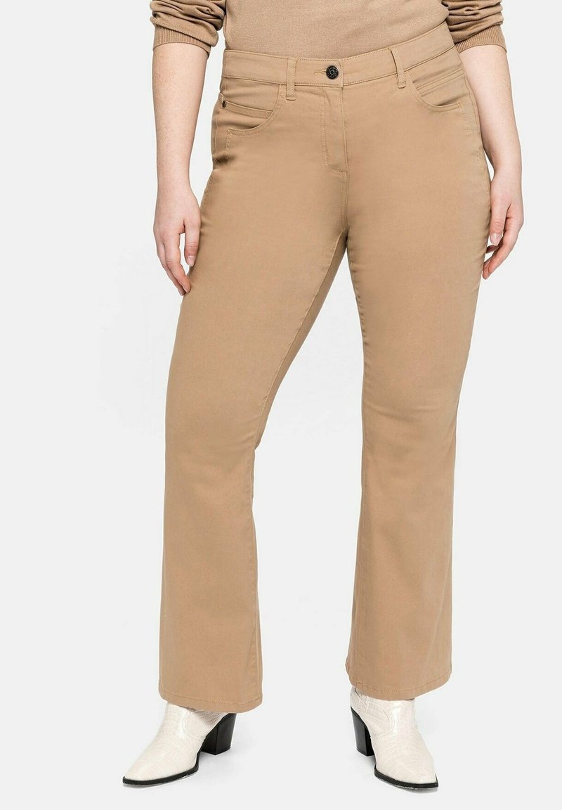 Beige, gerade geschnittene Hose mit Knopfverschluss, zwei Fronttaschen, glatter Textur und kombiniert mit weißen Stiefeletten mit Absatz im Krokodilmuster.