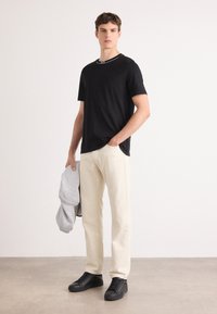Svart t-skjorte med korte ermer og hvit hals, beige rette bukser, grå mønstret jakke og svarte joggesko. Jevne stoffteksturer.