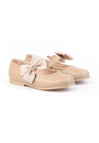Zapatos beige de niña estilo Mary Jane con cierre y grandes lazos de tela a juego en cada zapato, mostrados sobre un fondo blanco.