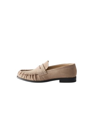 Mocassin beige en daim à enfiler avec une semelle noire et une couture moc toe, présenté de côté sur fond blanc.
