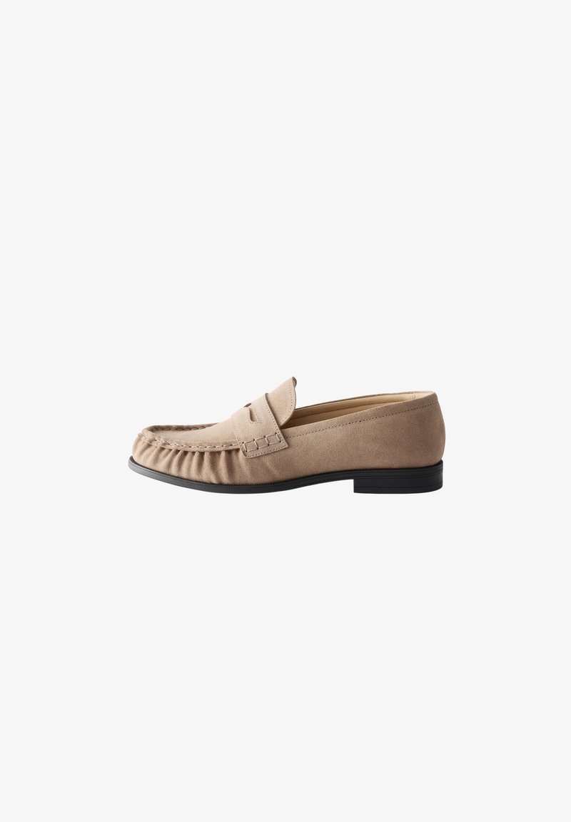Mocassin beige en daim à enfiler avec une semelle noire et une couture moc toe, présenté de côté sur fond blanc.