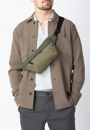 Skuldertaske i olivengrøn, lavet af holdbart materiale med et slankt rektangulært design og en justerbar rem for behagelig bæring.