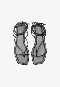 Sorte flate sandaler med et slankt, kryss-design. Kvadratisk tå og minimalistisk estetikk. Glatt, matt finish på innersålen.
