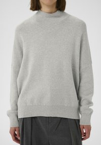 Maglione grigio chiaro in maglia con collo alto, spalle scese e maniche lunghe. Texture morbida, vestibilità rilassata e dettaglio a coste sull'orlo.