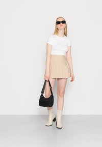 T-shirt branco cropped, saia mini em xadrez bege com pregas, bolsa de ombro preta e botas cream até ao joelho com salto bloco. Óculos de sol pretos.
