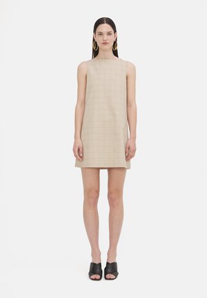 Μπεζ καρό μίνι φόρεμα με ίσια γραμμή, χωρίς μανίκια και μαλακή υφή. Φορεμένο με μαύρες ανοιχτές μπότες και μεγάλα σκουλαρίκια κρίκοι.