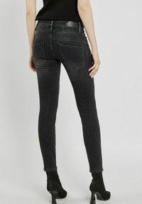 Czarne, obcisłe dżinsy o gładkiej fakturze, wysoki stan i dwie ukośne tylne kieszenie. Stylizowane z czarnymi, wysokimi botkami za kostkę.