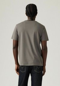 Grå kortærmet t-shirt med rund hals, glat tekstur, parret med mørke denimjeans med baglommer, der har en syet logo-detalje.