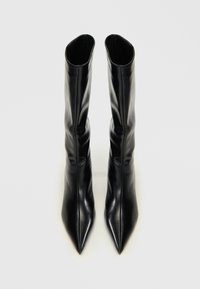 Botas de cuero negro hasta la rodilla con un diseño de puntera afilada, que presentan una textura suave y una silueta elegante, sin herrajes ni adornos visibles.