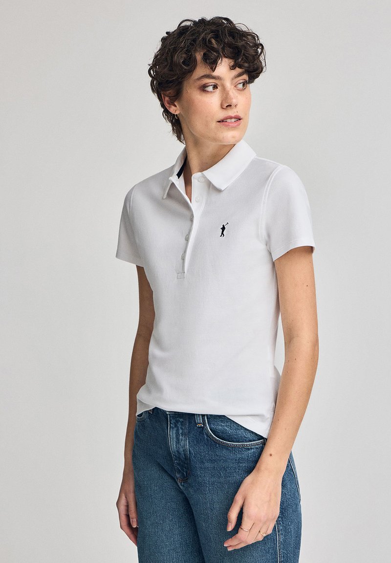 Polo shirt blanc en tissu lisse, avec un rabat à trois boutons et un petit logo noir brodé sur la poitrine gauche.