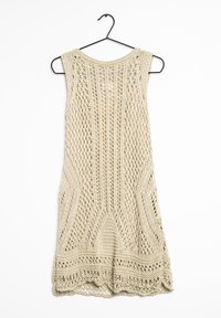 Robe sans manches au crochet beige clair, avec un design ajouré comprenant des motifs géométriques et un ourlet festonné. Accrochée à un crochet noir.