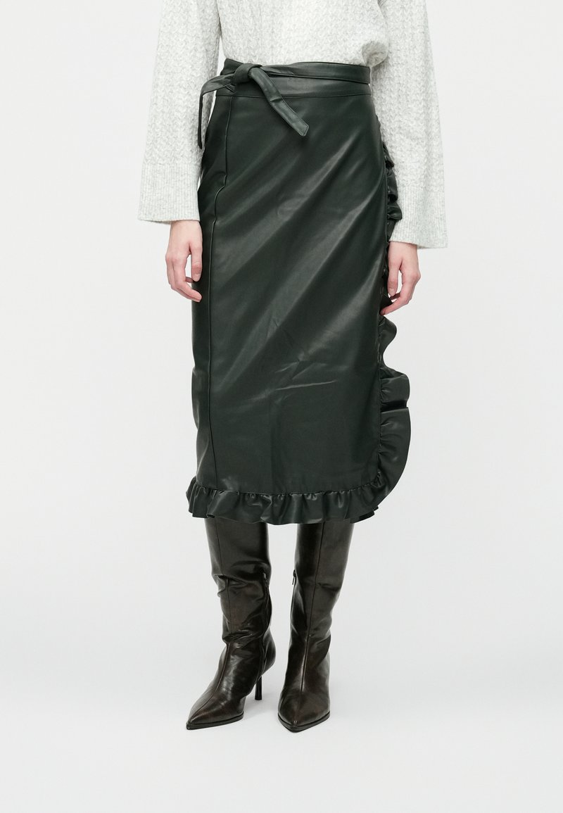 Dark green leather midi skirt with a ruffled hem, belted waist, and smooth texture. Paired with fitted, shiny brown knee-high boots.