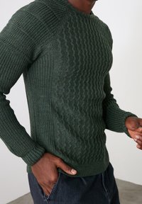 Donkergroene gebreide trui met textuurpatronen en geribbelde manchetten. Heeft een ronde hals en een aansluitend ontwerp, gemaakt van zachte stof.