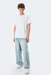 Hvid bomulds T-shirt med korte ærmer, parret med lyseblå vidde bukser. Hvide sneakers fuldender outfittet.