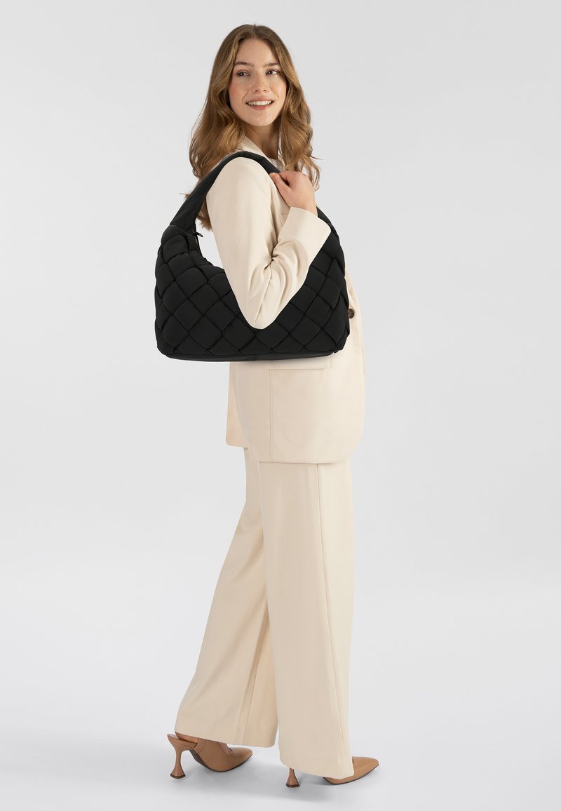 Schwarze, gesteppten Stoff-Handtasche im Hobo-Stil, mit breitem Schulterriemen und diagonalen Musterdetails, vor einem hellen Hintergrund präsentiert.