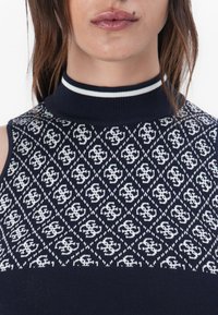 Débardeur sans manches en tricot marine avec un motif géométrique blanc, un col haut avec une bande blanche en accent, et une finition texturée.