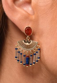 Boucles d'oreilles en métal doré avec un cabochon rouge et un design en forme d'éventail, ornées de perles bleues et rouges ainsi que d'accents en verre transparent, suspendues à un anneau.