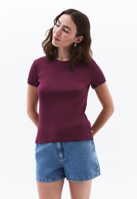T-shirt bordeaux a maniche corte con scollatura rotonda e texture liscia, abbinato a pantaloni corti in denim azzurro.