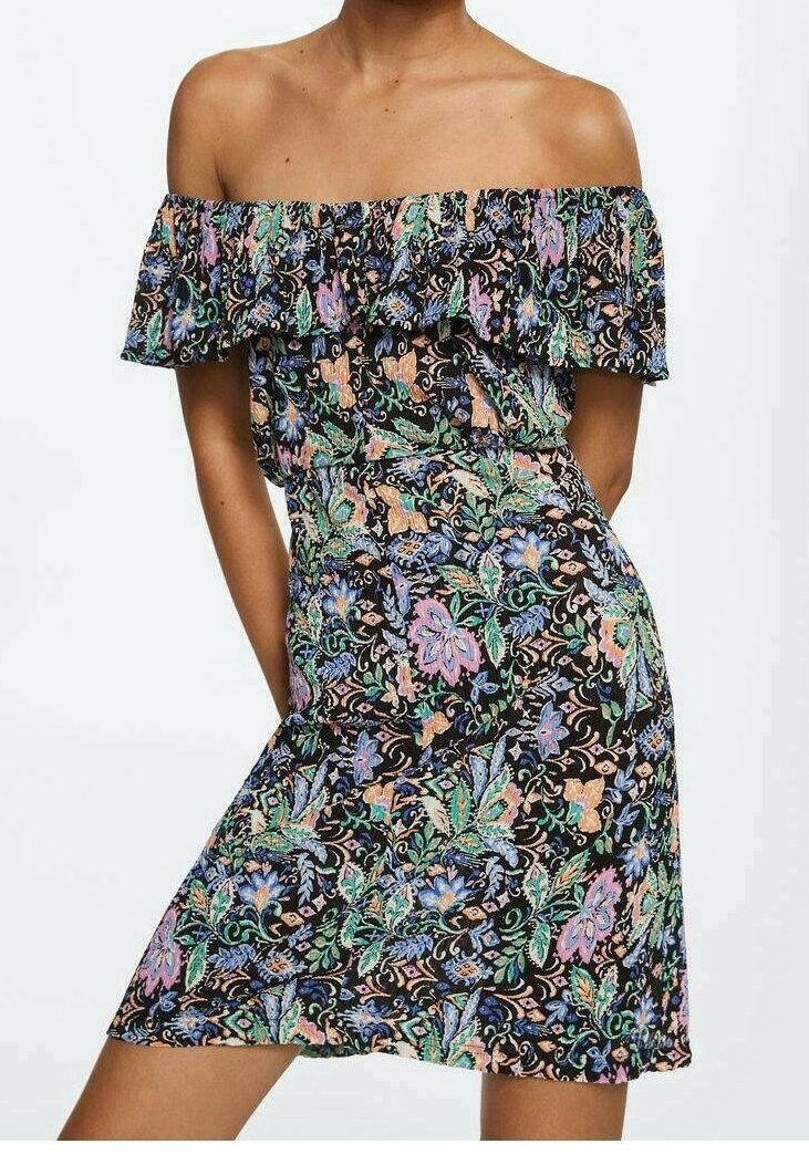 Robe épaules dénudées avec encolure froncée en tissu noir à motifs floraux et feuillages colorés, portée avec les bras le long du corps et un genou légèrement fléchi.